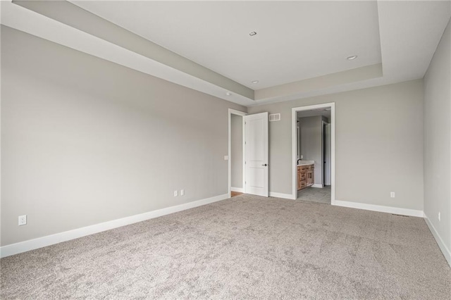 unfurnished bedroom featuring baseboards, light carpet, a tray ceiling, and visible vents