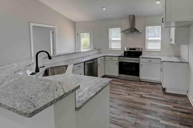 kitchen featuring stainless steel appliances, sink, wall chimney range hood, kitchen peninsula, and tasteful backsplash