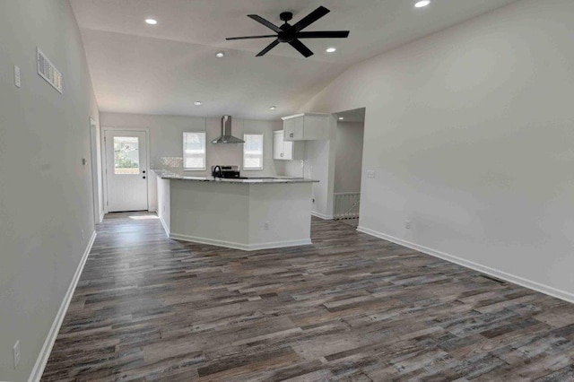 kitchen with white cabinetry, wall chimney range hood, dark wood-type flooring, ceiling fan, and a kitchen island with sink