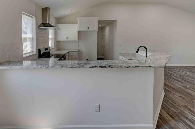 kitchen featuring wall chimney exhaust hood, lofted ceiling, backsplash, and white cabinets