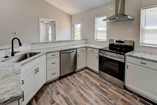 kitchen featuring backsplash, stainless steel appliances, sink, lofted ceiling, and wall chimney range hood