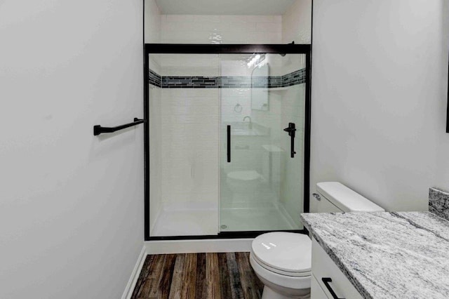 bathroom featuring vanity, toilet, wood-type flooring, and a shower with door