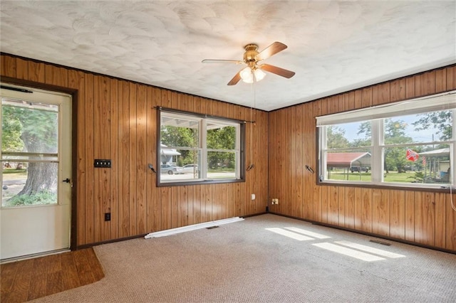 carpeted spare room featuring wood walls and ceiling fan