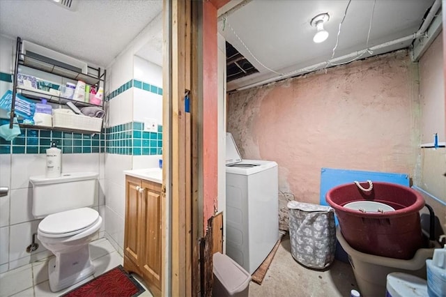 bathroom with vanity, a washtub, washer / dryer, tile walls, and toilet