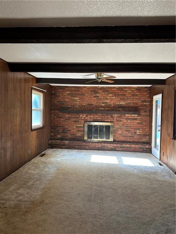 unfurnished living room with beam ceiling, ceiling fan, light colored carpet, and a brick fireplace