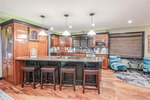 kitchen featuring a breakfast bar area, light wood-style flooring, built in microwave, decorative backsplash, and dark stone countertops