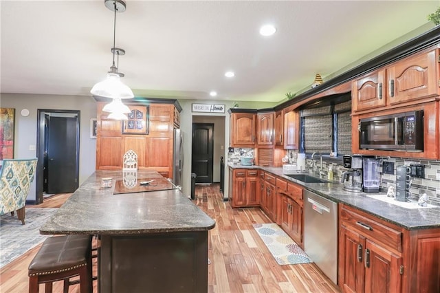 kitchen with appliances with stainless steel finishes, a sink, light wood finished floors, and tasteful backsplash