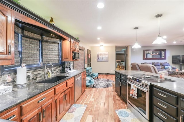 kitchen with a sink, appliances with stainless steel finishes, light wood-type flooring, backsplash, and decorative light fixtures