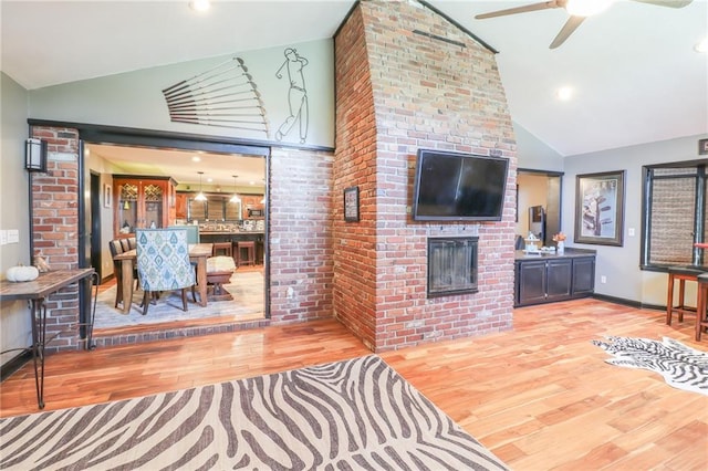 living room with a brick fireplace, a ceiling fan, high vaulted ceiling, and wood finished floors