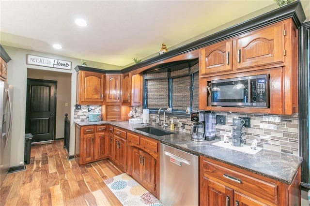 kitchen with a sink, light wood-style floors, appliances with stainless steel finishes, brown cabinets, and tasteful backsplash