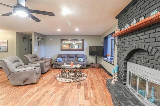 living room with a fireplace, visible vents, a ceiling fan, a textured ceiling, and wood finished floors