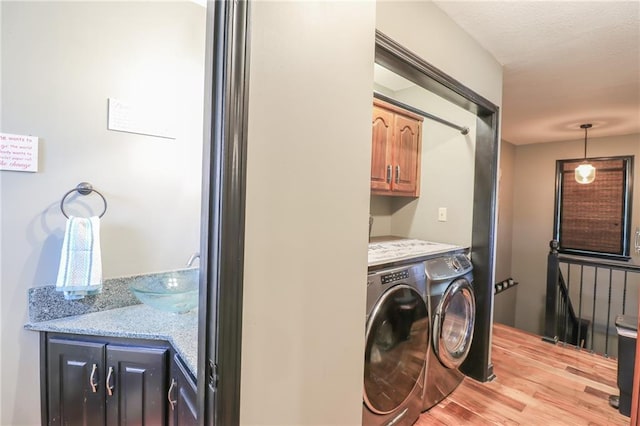 laundry room with washer and dryer, cabinet space, a sink, and light wood finished floors