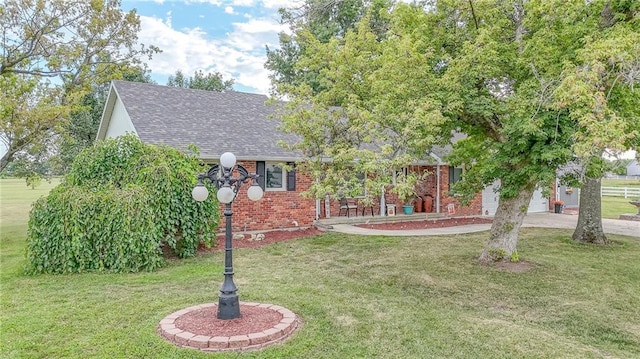 view of front of property featuring a shingled roof, brick siding, driveway, and a front lawn