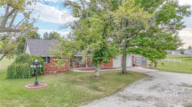 view of property hidden behind natural elements with brick siding, fence, roof with shingles, a front lawn, and gravel driveway