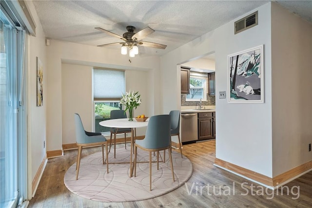 dining room with light wood-type flooring, a textured ceiling, and a wealth of natural light