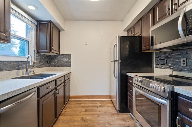 kitchen with dark brown cabinetry, sink, tasteful backsplash, stainless steel appliances, and light hardwood / wood-style floors