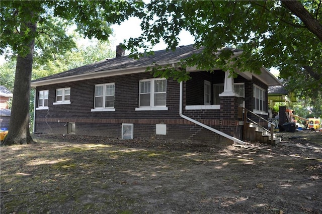 view of side of home featuring covered porch, brick siding, and a chimney