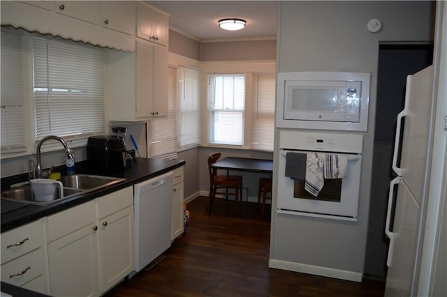 kitchen with white appliances, dark wood-type flooring, a sink, white cabinets, and dark countertops