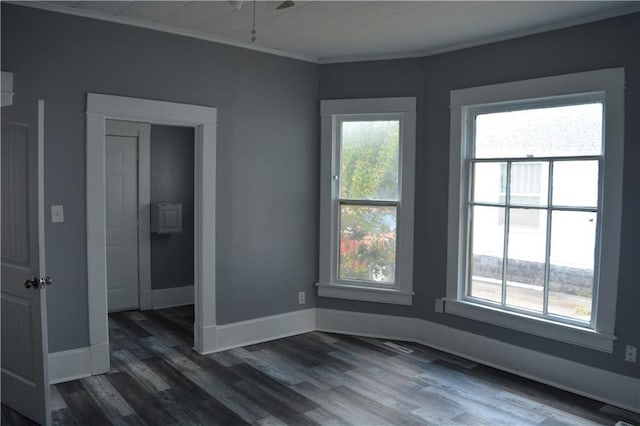 unfurnished room featuring crown molding, baseboards, dark wood finished floors, and a wealth of natural light