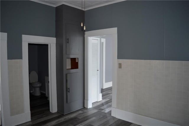 corridor featuring ornamental molding, dark wood finished floors, and tile walls