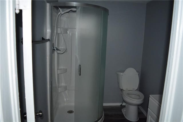 bathroom with toilet, a shower stall, baseboards, and wood finished floors