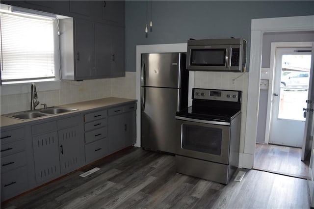 kitchen with dark wood-type flooring, a sink, stainless steel appliances, light countertops, and backsplash