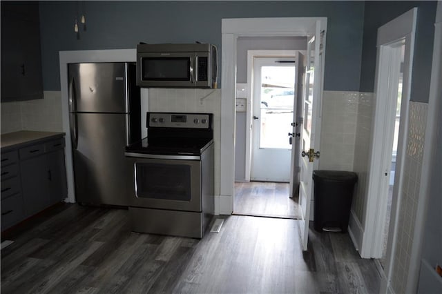 kitchen with dark wood-style floors, stainless steel appliances, tile walls, and a wainscoted wall