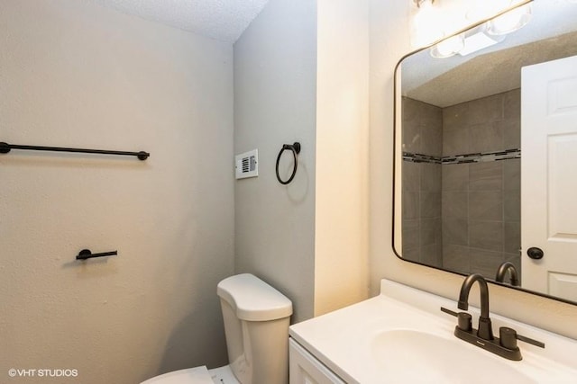 bathroom featuring tiled shower, vanity, toilet, and a textured ceiling