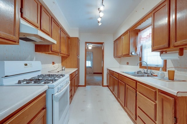 1040 Stone Ave, Independence, MO 64055 - kitchen with white gas stove, a sink, under cabinet range hood, healthy amount of natural light, and wallpapered walls
