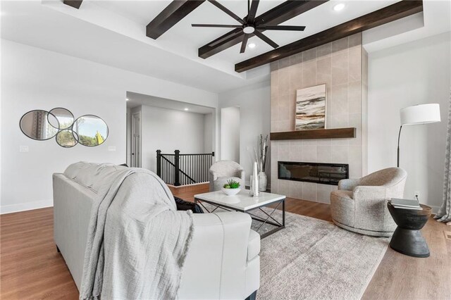 living room featuring ceiling fan, a fireplace, beam ceiling, and wood-type flooring