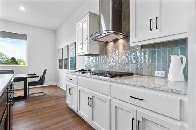 kitchen featuring stainless steel gas cooktop, backsplash, dark hardwood / wood-style flooring, wall chimney exhaust hood, and white cabinets