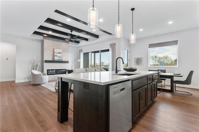 kitchen with a fireplace, a sink, wood finished floors, stainless steel dishwasher, and an island with sink