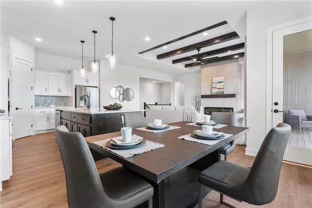 dining area with ceiling fan, a tile fireplace, beam ceiling, and light hardwood / wood-style floors