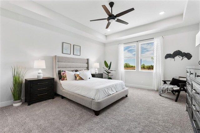 bedroom featuring a raised ceiling, ceiling fan, and light colored carpet