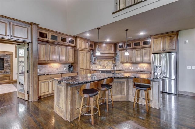 kitchen featuring dark hardwood / wood-style flooring, stainless steel fridge with ice dispenser, a center island with sink, and a breakfast bar