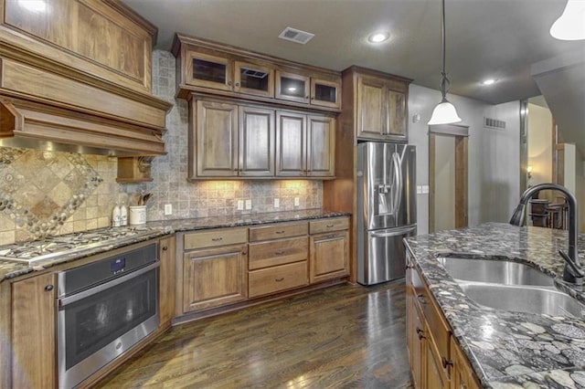 kitchen featuring appliances with stainless steel finishes, dark hardwood / wood-style flooring, dark stone counters, sink, and decorative light fixtures