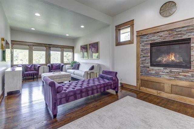 living room with a stone fireplace and dark wood-type flooring