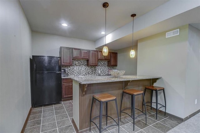 kitchen featuring tasteful backsplash, kitchen peninsula, black fridge, and pendant lighting