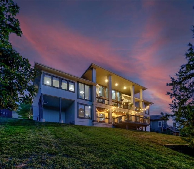 back house at dusk with a yard and a balcony