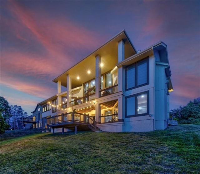 back house at dusk with a lawn and a balcony