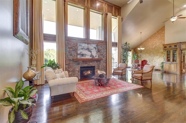 living room featuring ceiling fan with notable chandelier, a fireplace, high vaulted ceiling, and dark wood-type flooring