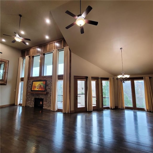 unfurnished living room with a fireplace, dark hardwood / wood-style flooring, ceiling fan with notable chandelier, and a healthy amount of sunlight