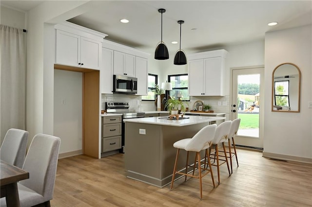 kitchen featuring pendant lighting, light wood-type flooring, a center island, white cabinetry, and stainless steel appliances