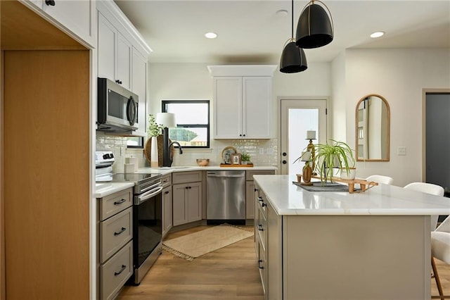 kitchen with white cabinets, appliances with stainless steel finishes, light wood-type flooring, and tasteful backsplash