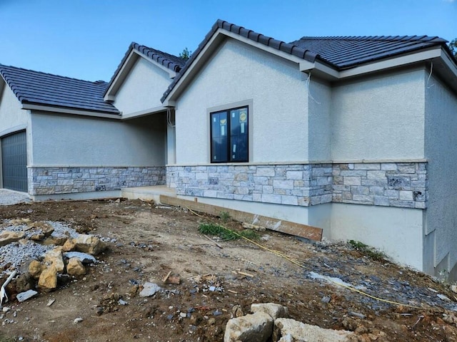 view of side of home with a garage, stone siding, and stucco siding