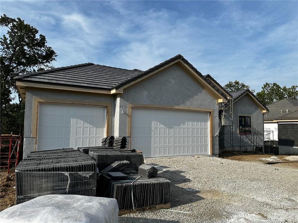 view of front of house with an outbuilding, a tile roof, stucco siding, an attached garage, and driveway