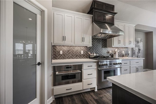 kitchen with wall chimney exhaust hood, backsplash, dark wood-type flooring, stainless steel appliances, and white cabinetry