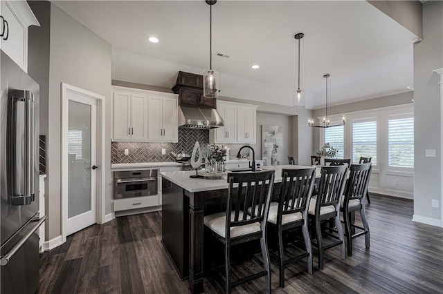 kitchen with stainless steel appliances, white cabinetry, an island with sink, dark wood-type flooring, and exhaust hood