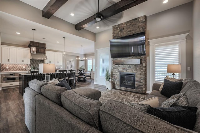 living room with a stone fireplace, dark hardwood / wood-style floors, beamed ceiling, and an inviting chandelier