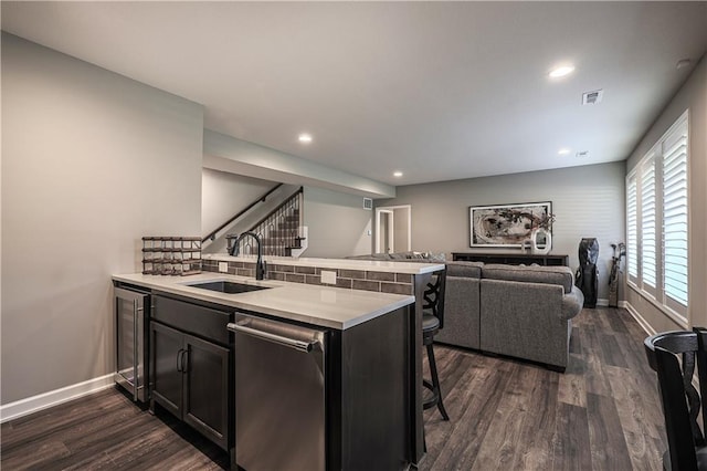 kitchen with a kitchen bar, dark wood-type flooring, kitchen peninsula, sink, and stainless steel dishwasher